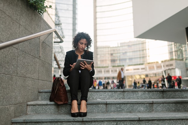 Mujer trabajando con su tablet en la ciudad, sentada sobre unos escalones.