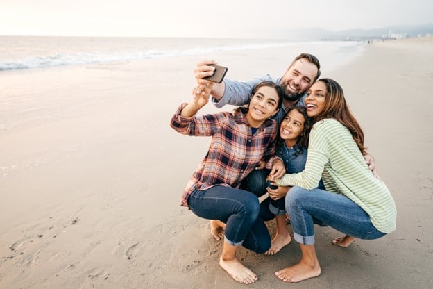 Dos niños con sus padres tomando una selfie grupal en la playa.