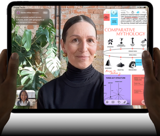 iPad Pro, exterior frontal, orientación horizontal, color negro espacial, esquinas redondeadas, bisel de pantalla negro, manos sosteniendo los lados derecho e izquierdo, pantalla que muestra una conversación en FaceTime que se traduce en vivo y una app educativa que muestra una presentación de "Comparative Mythology" con texto, diagramas y notas escritas a mano