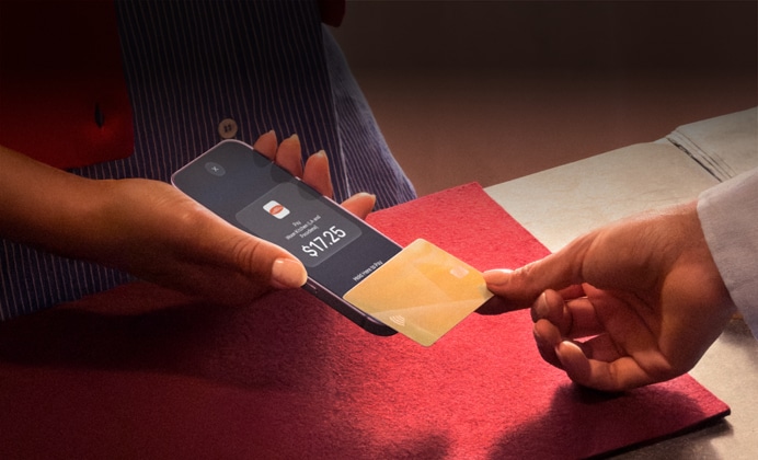 Una mano acerca una tarjeta de crédito a un iPhone para completar un pago