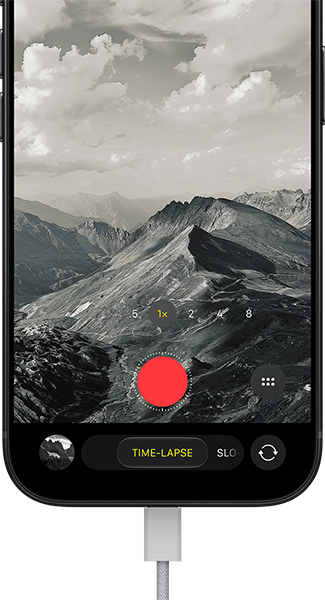 iPhone 18 Pro, vista frontal exterior, se muestra un paisaje montañoso, con la superposición del modo de cámara en modo Time-Lapse, y el cable de alimentación conectado al puerto de carga