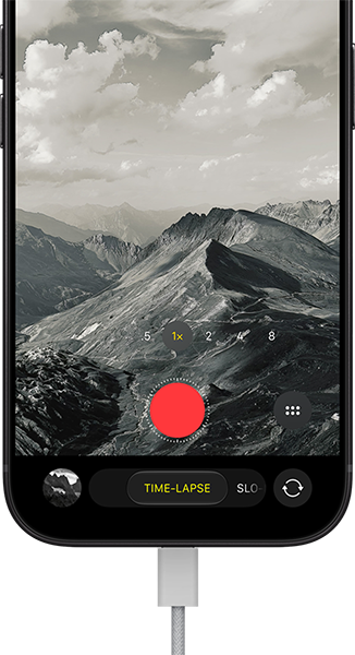 iPhone 18 Pro, vista frontal exterior, se muestra un paisaje montañoso, con la superposición del modo de cámara en modo Time-Lapse, y el cable de alimentación conectado al puerto de carga