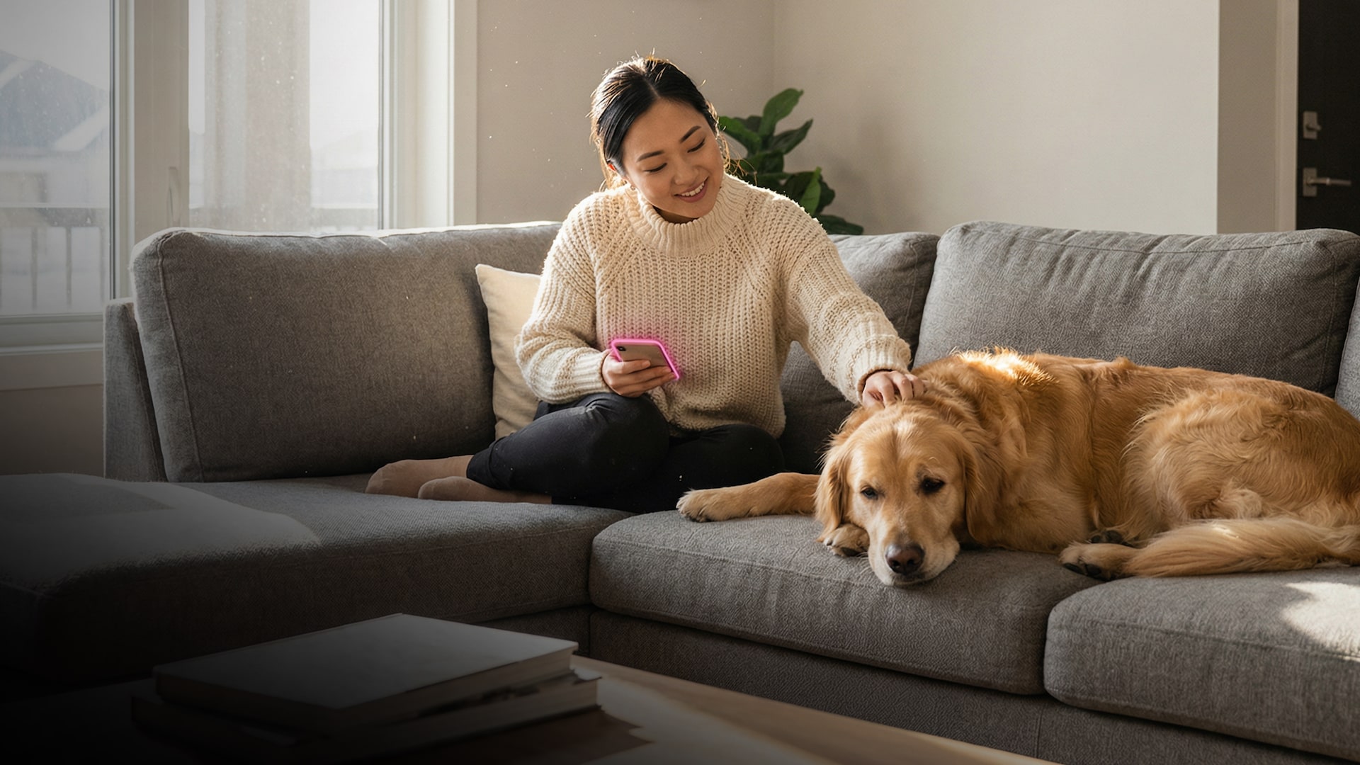 Una mujer está en el sofá acariciando a su perro y sostiene el móvil, que emite un brillo magenta de T-Mobile.