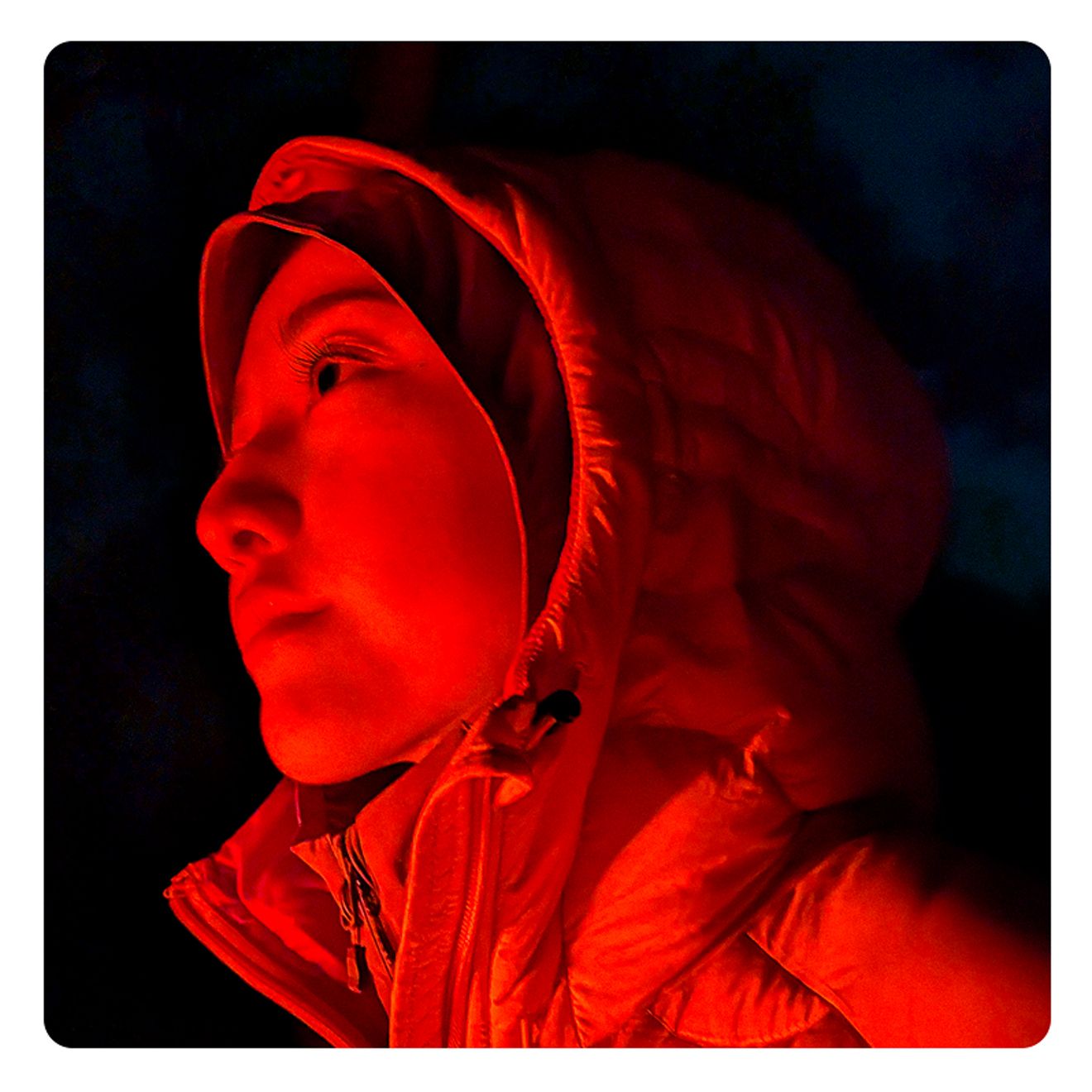 Primer plano de una persona abrigada con una parka, iluminada de forma dramática por la noche