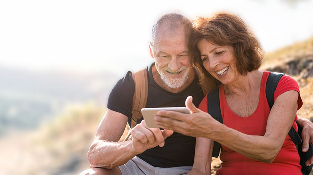 Una pareja de personas mayores mira un teléfono mientras hace senderismo.