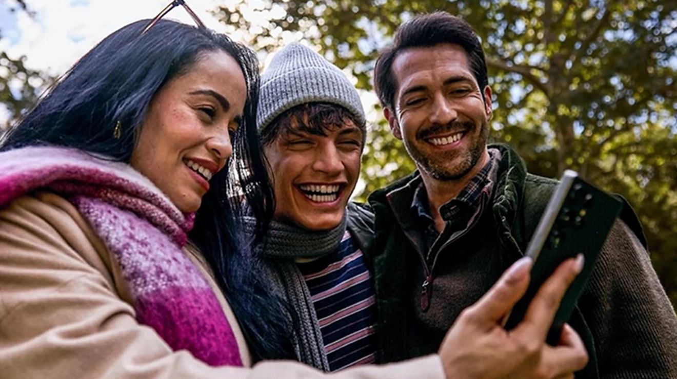 Tres personas miran juntas un teléfono mientras están al aire libre.