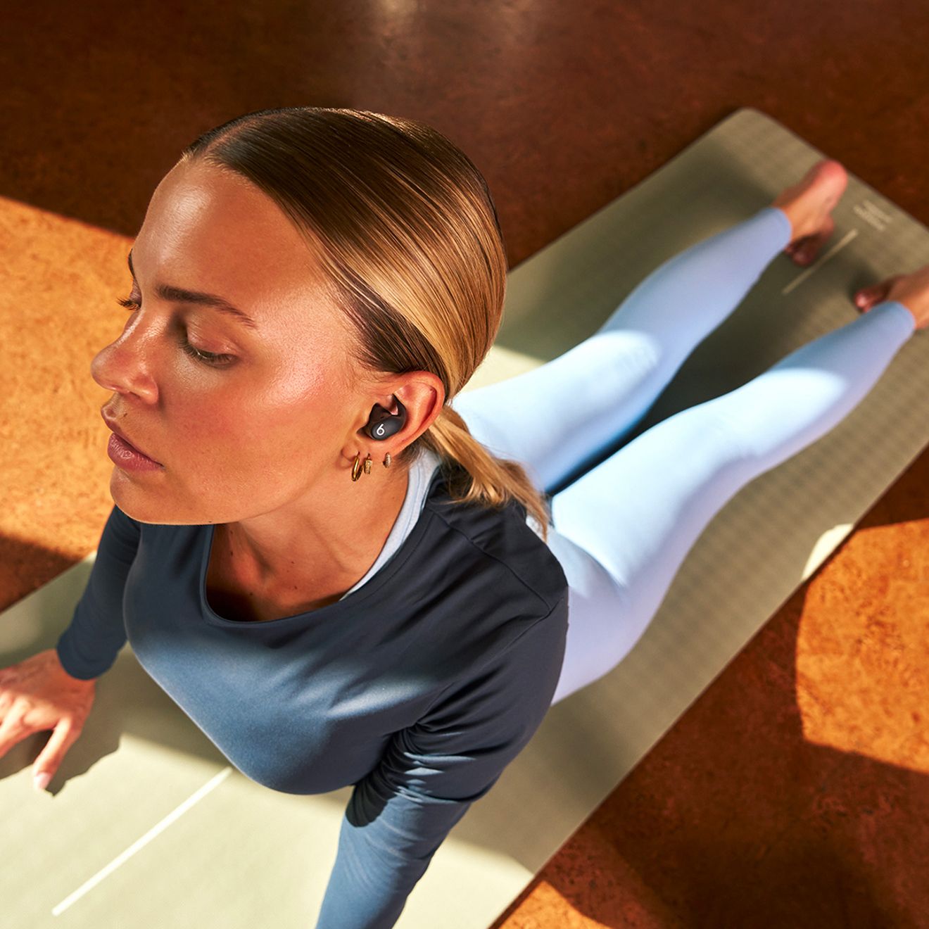 Una mujer está haciendo ejercicio y estiramientos con sus Beats Powerbeats Fit puestos.