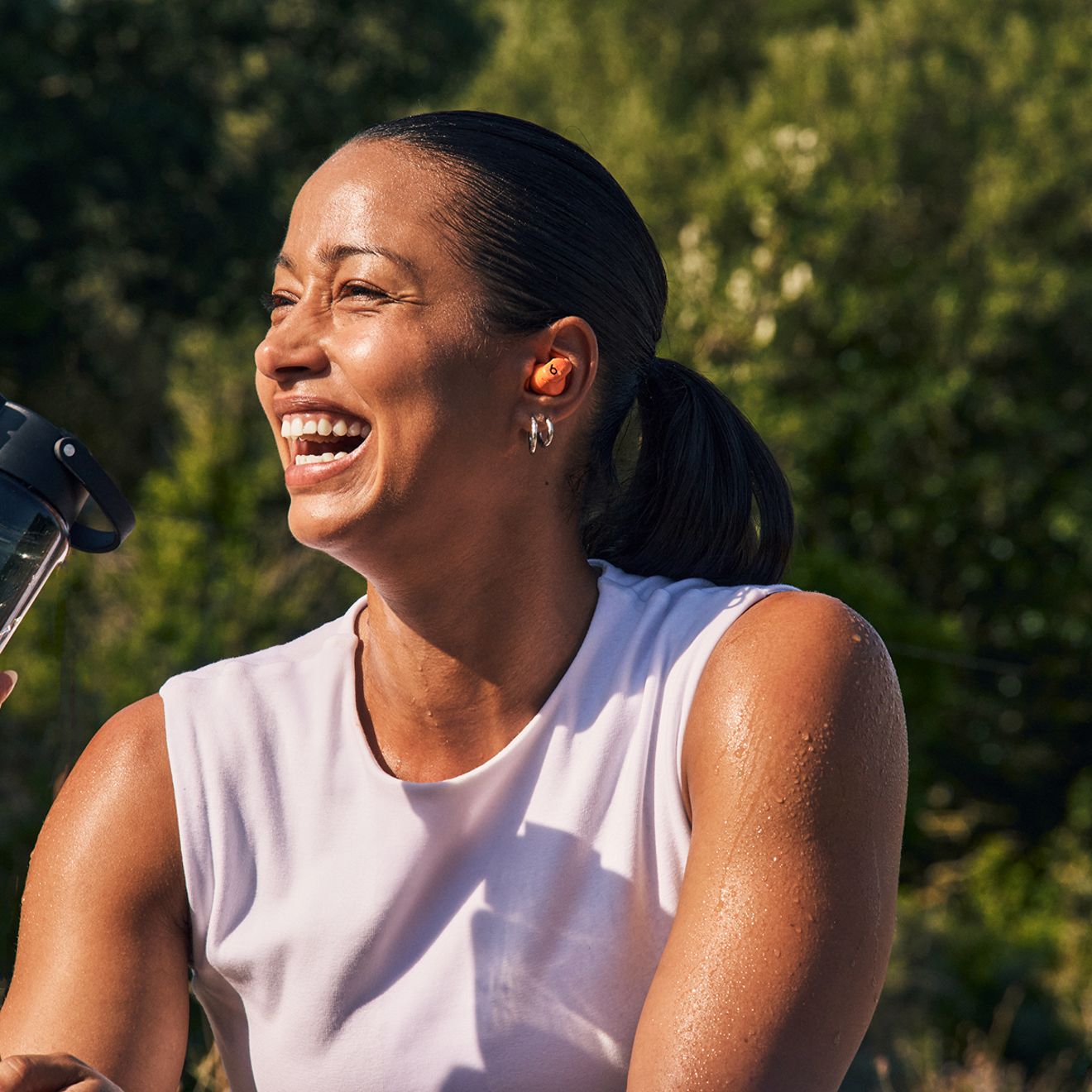 Una mujer sonríe mientras está al aire libre escuchando sus Beats Powerbeats Fit.