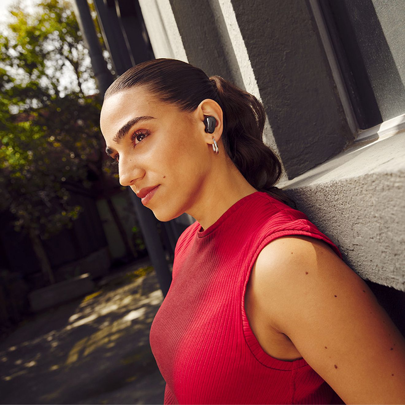 Una mujer apoyada contra una pared al aire libre mientras escucha sus audífonos Bose Quiet Comfort Ultra de segunda generación.