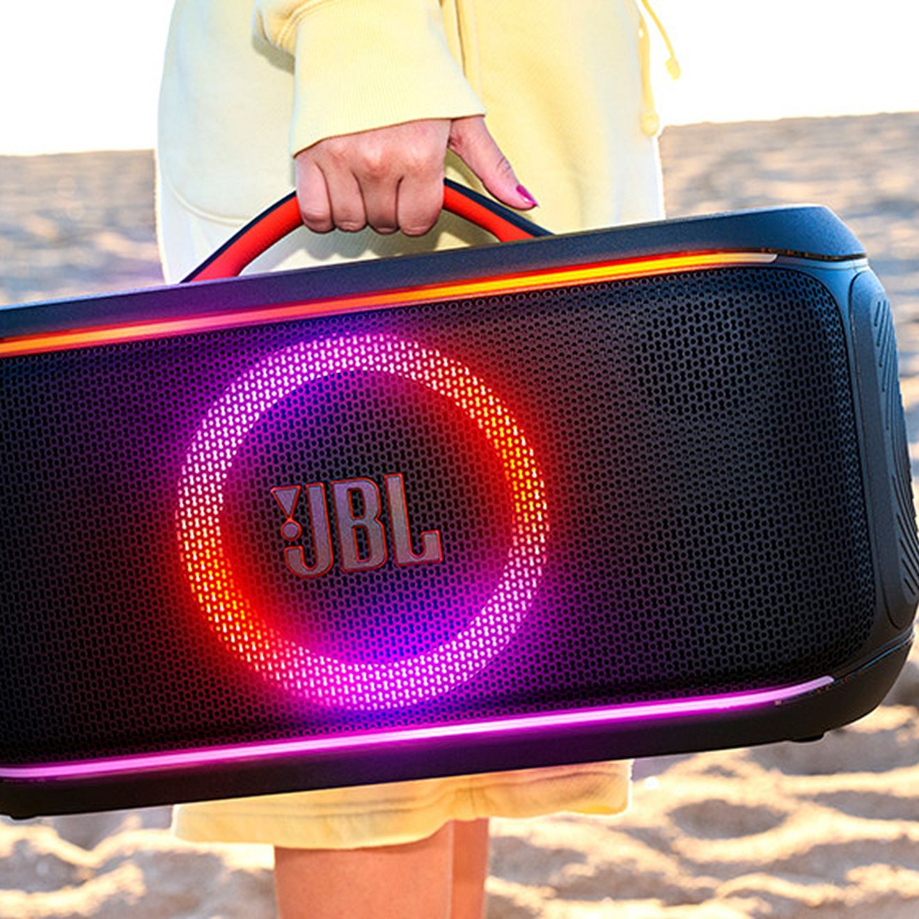 Alguien lleva una JBL PartyBox On-the-Go 2 mientras camina por la playa hacia su destino.