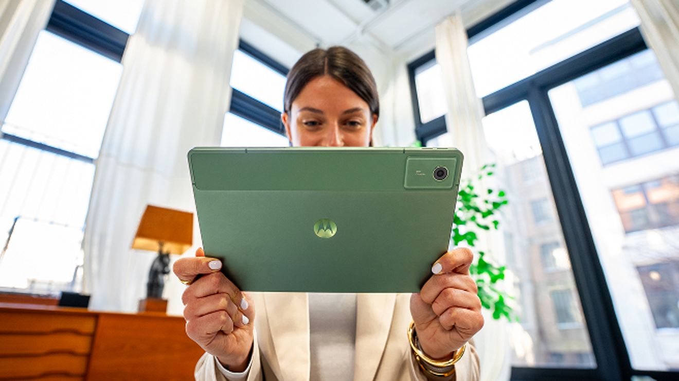 Mujer sentada en interiores que sostiene una moto pad verde horizontalmente con ambas manos, con la parte posterior de la tablet y el logotipo centrado de Motorola de cara a la cámara.