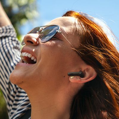 Una mujer sonriente con audífonos JBL Vibe Beam dos.