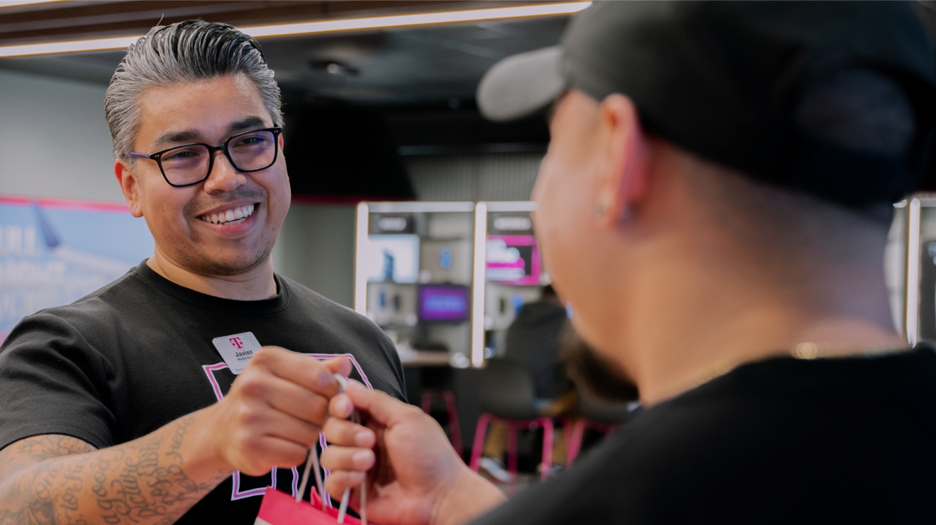 Vendedor de T-Mobile entregando una bolsa de compras a un cliente.