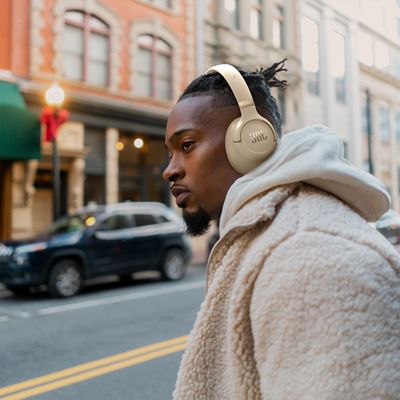 Un hombre con audífonos JBL Tune 780NC cruza una calle muy transitada.