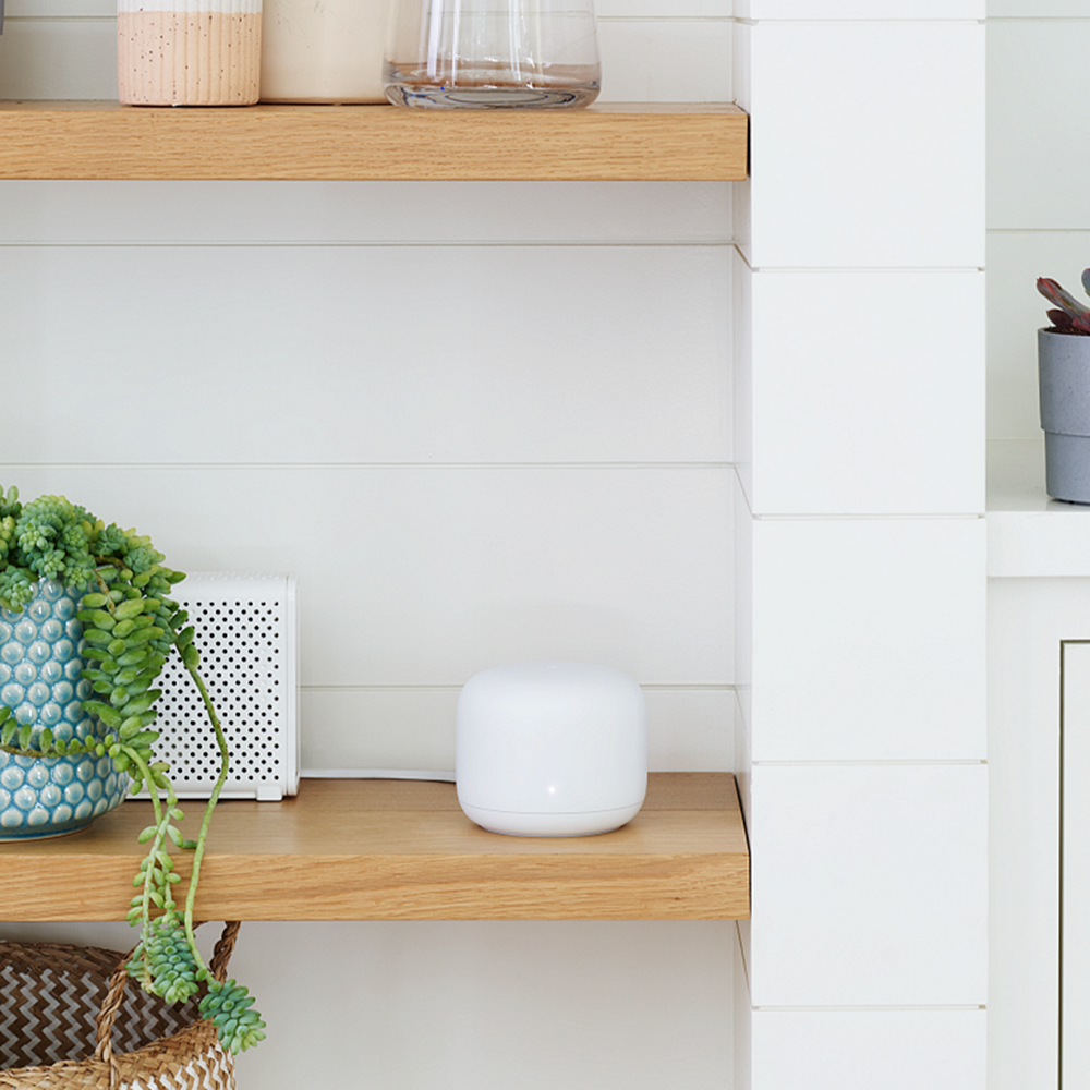 Un enrutador Google Nest en un estante junto a una planta en una maceta decorativa.