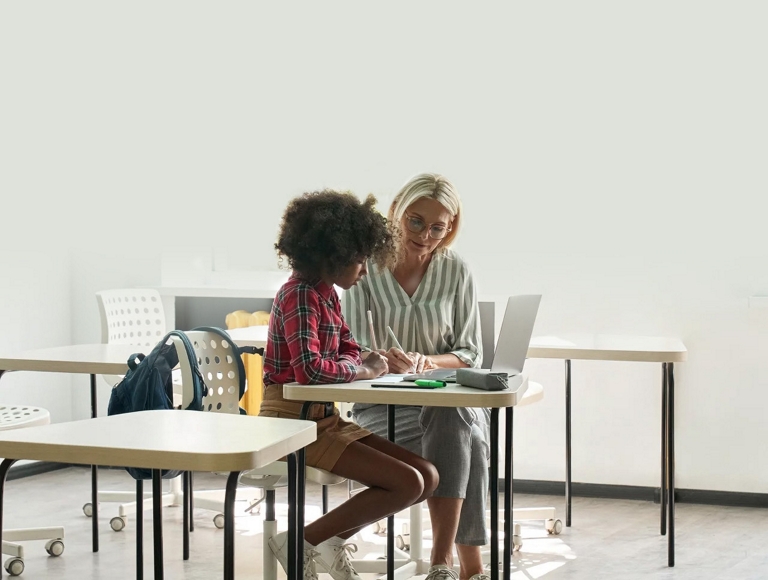 Docente y estudiante trabajan juntos en una laptop en un salón de clases