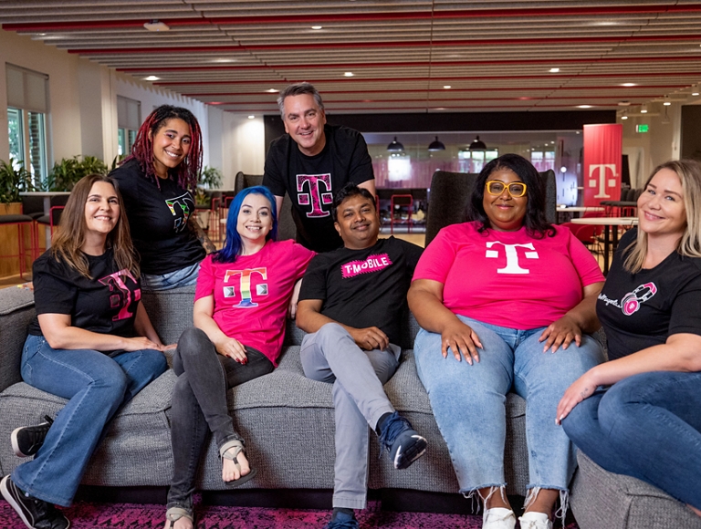 Un grupo diverso de empleados de T-Mobile sonríen sentados en un sofá.