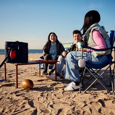 Dos mujeres y un hombre están en la playa escuchando música con un JBL Clip cinco.