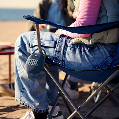Un JBL Clip cinco cuelga de la silla de una mujer en la playa.