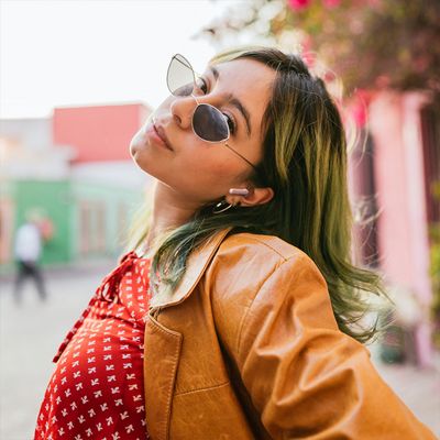 Una mujer con audífonos JBL Vibe Beam dos inclina un poco la cabeza y posa en la calle.