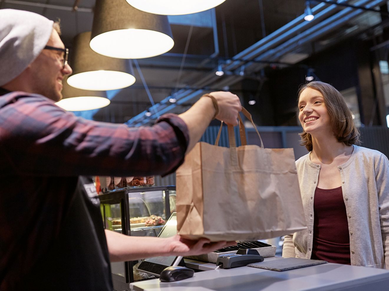Empleado entregando una bolsa de la compra a un cliente sonriente.