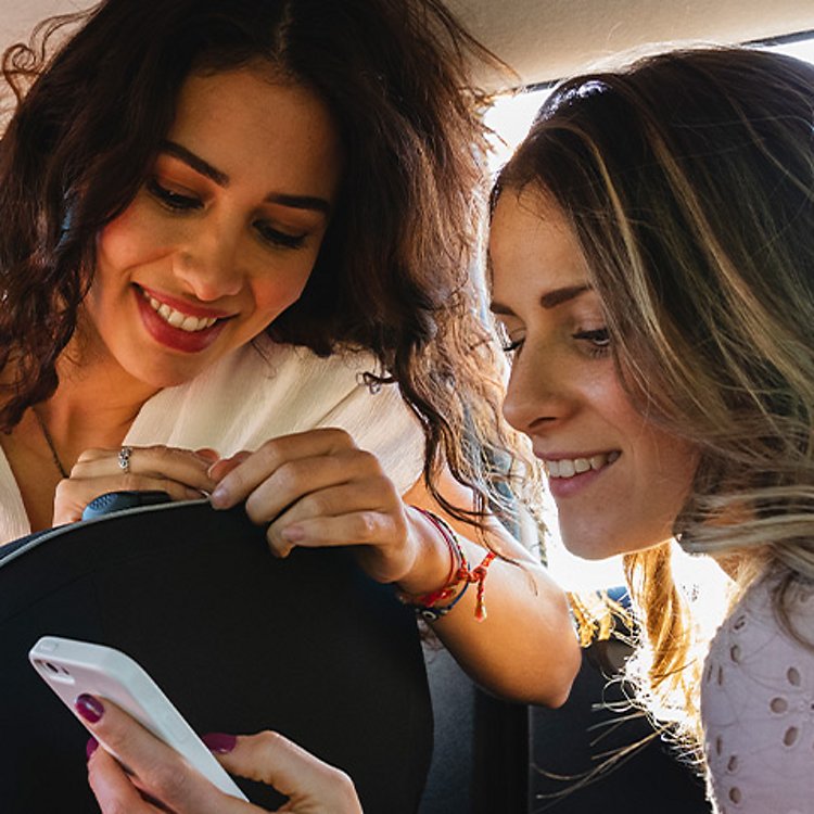 Dos mujeres en un auto mirando un teléfono