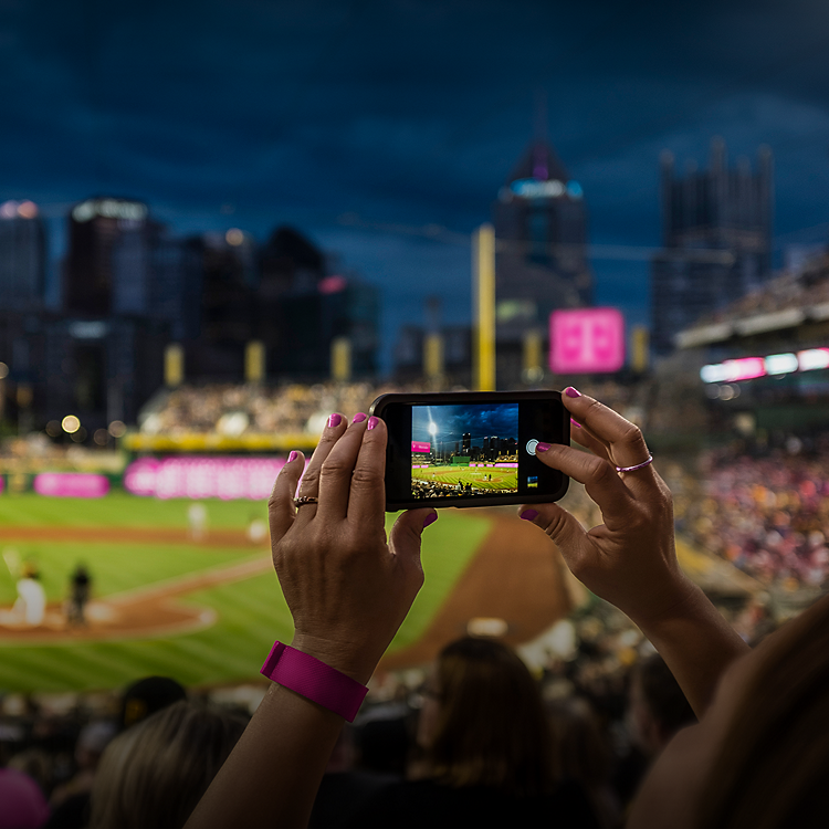 En un estadio de béisbol, dos manos sostienen un teléfono grabando un partido de béisbol de Las Grandes Ligas.