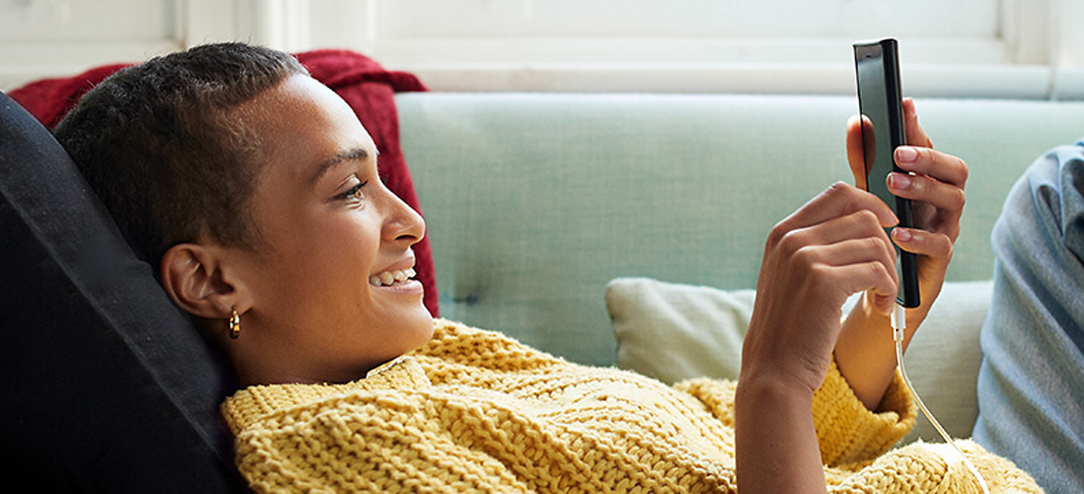 Una mujer tumbada en el sofá sonriendo mientras mira su teléfono