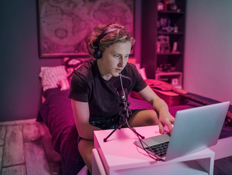 Joven adulto utilizando una laptop y equipo de audio en su dormitorio.