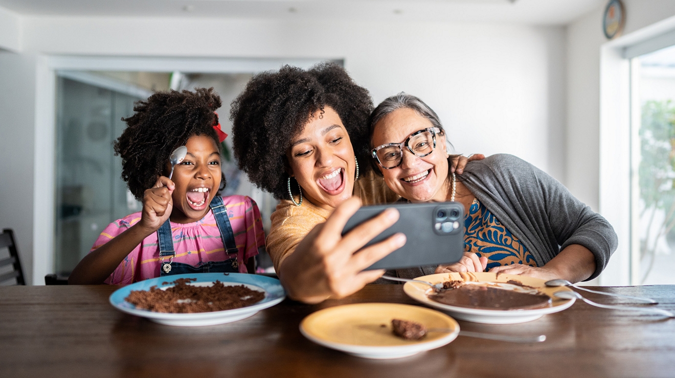 Una familia multigeneracional de tres miembros se toma un selfie reunida en torno a la mesa del comedor.