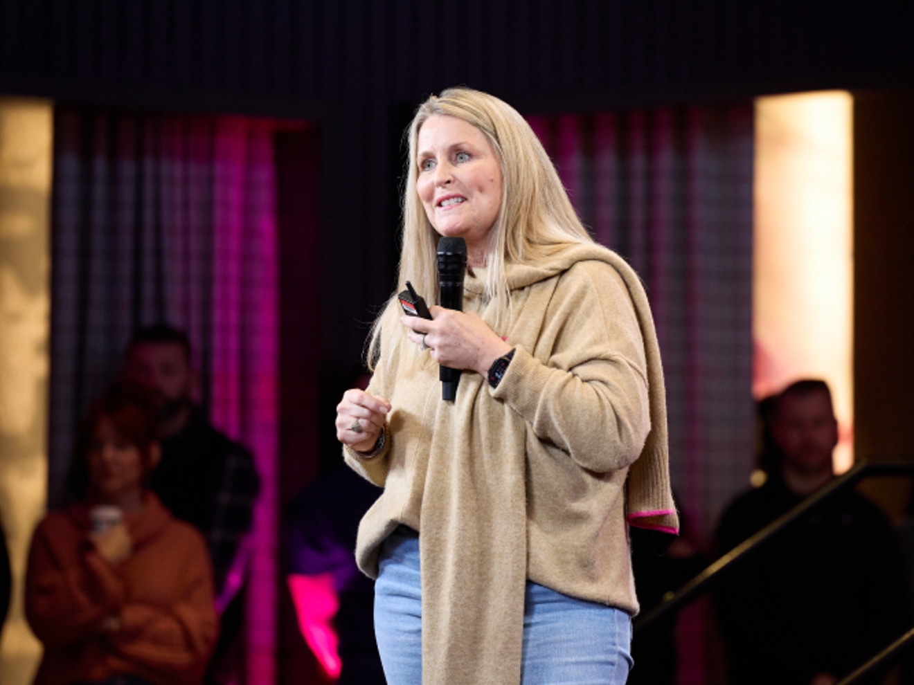 Deanne King sonriendo mientras habla a una multitud con un micrófono.