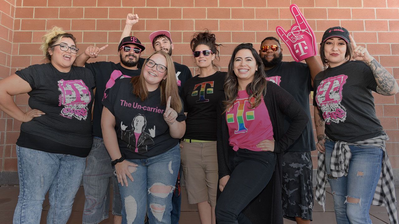 Hombres y mujeres posan alegremente luciendo camisetas de T-Mobile
