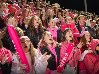 Un grupo de estudiantes vestidos de magenta animan desde las gradas.