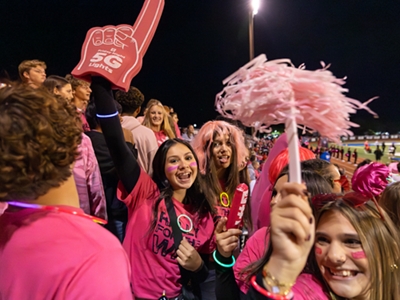 Un grupo de estudiantes vestidos de magenta animan desde las gradas.