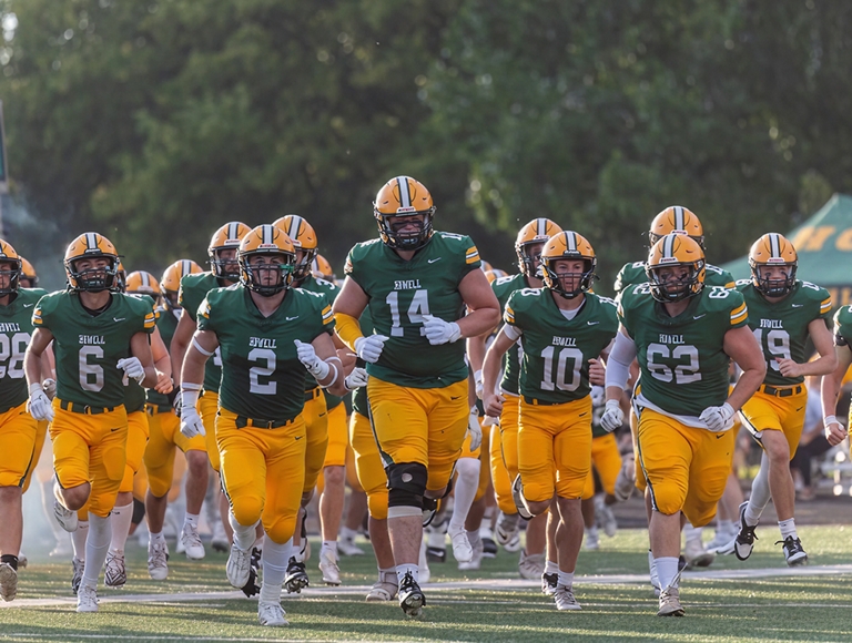 El equipo de fútbol de Howell High School, con uniformes de color verde y amarillo, corre en el campo durante un partido.
