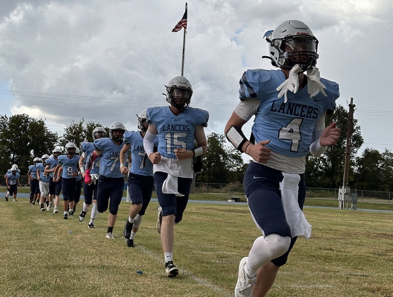 El equipo de fútbol de Southeast High School ​​​​​​, con uniformes de color celeste y azul marino, entrena afuera de la cancha antes de un partido.