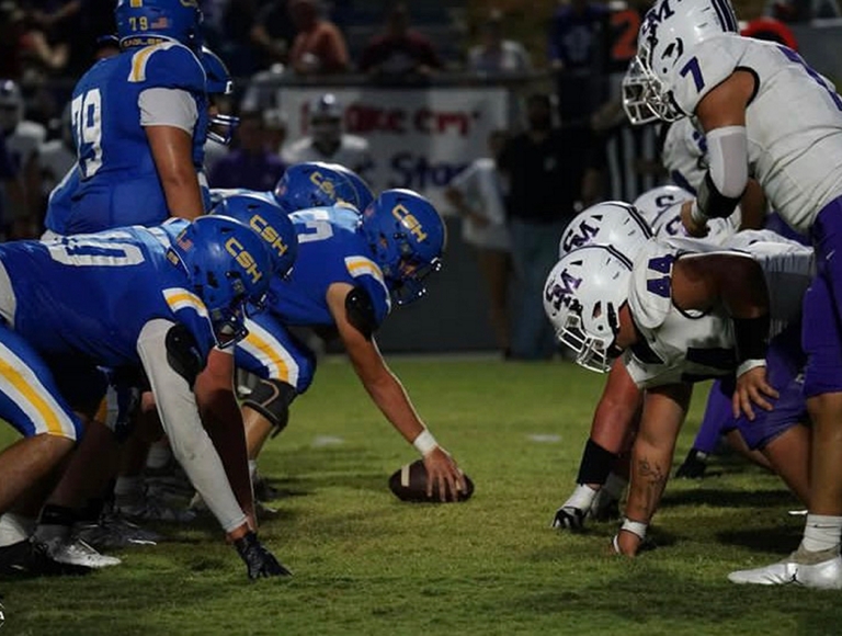 Los jugadores de fútbol de Susan Moore High School, con uniformes de color morado y blanco, toman su lugar en el campo al comienzo de un partido.