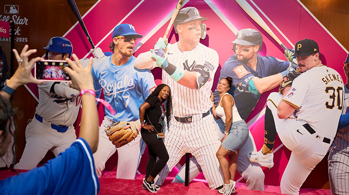 Dos amigos posando para una foto delante de un gran collage de jugadores de la MLB.