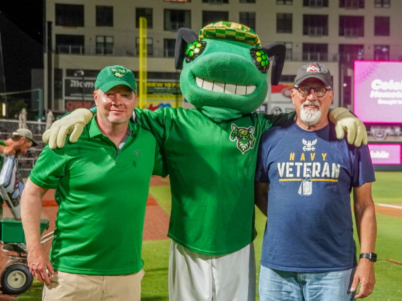 Bob Arnold, veterano de la Marina de EE. UU., posa junto a la mascota de un equipo de béisbol en un campo de béisbol.