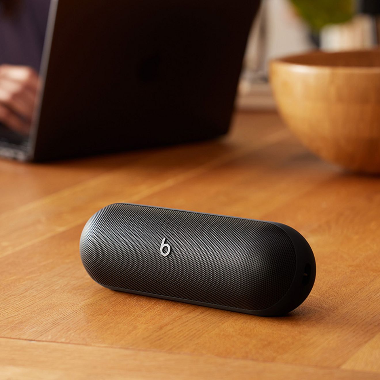 En primer plano se ve una beats pill negra, mientras alguien trabaja en su laptop.