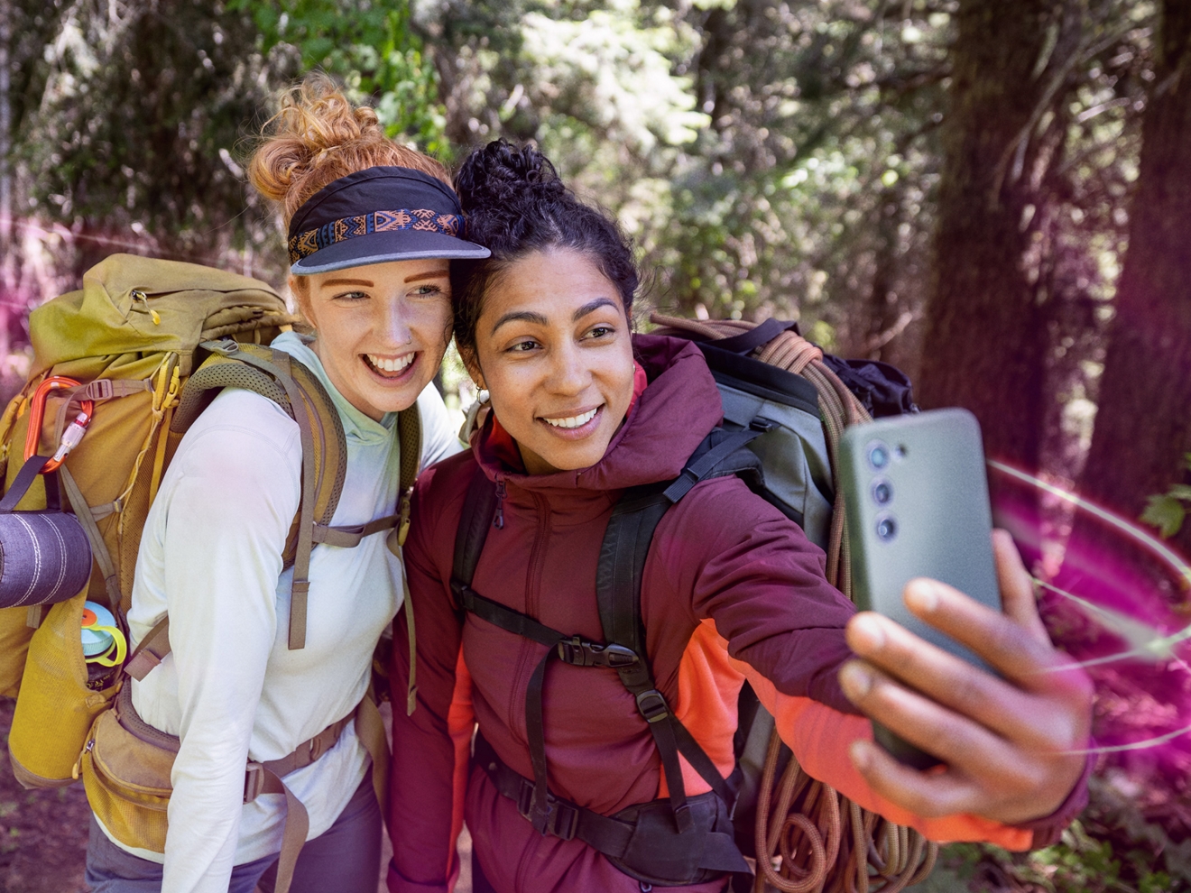 Una familia de cuatro personas mira un teléfono juntos en una playa rodeada de acantilados y pinos. Una banda de magenta los rodea.