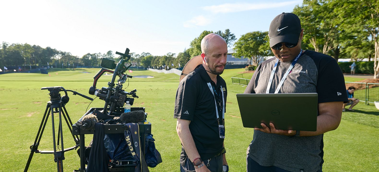 Two camera operators setting up their equipment on a golf course.