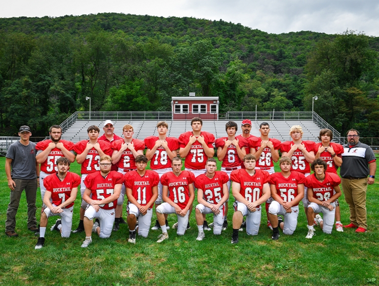 El equipo de fútbol de Bucktail High School, vestido con uniformes rojos y blancos, posa para una foto en su campo de fútbol.