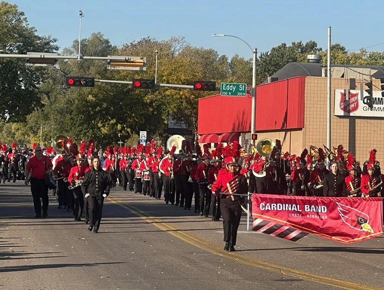 La banda musical de Crete High School, en atuendos de rojo y negro, desfilan por la calle durante un desfile.