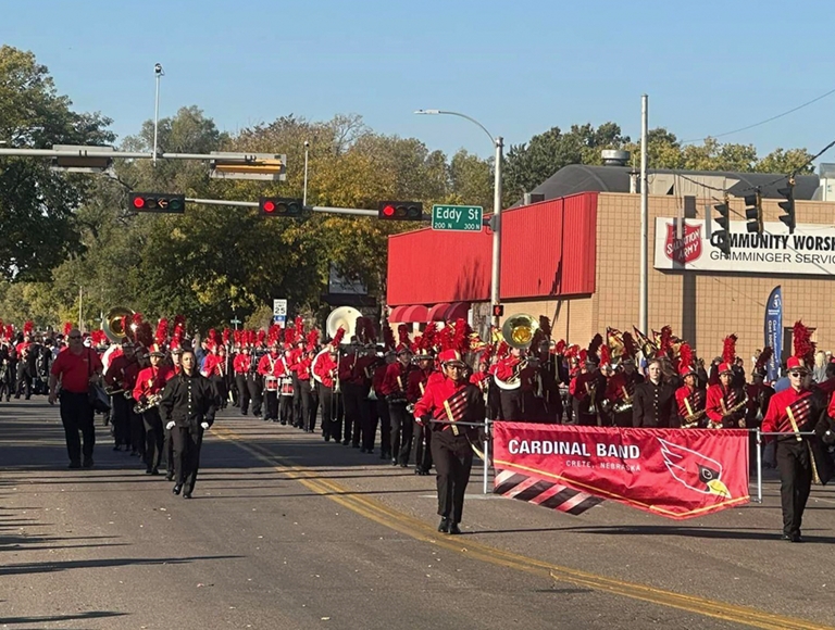 La banda musical de Crete High School, en atuendos de rojo y negro, desfilan por la calle durante un desfile.