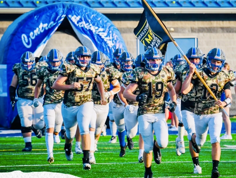 El equipo de fútbol de Central Mountain High School corre hacia el campo agitando una bandera.
