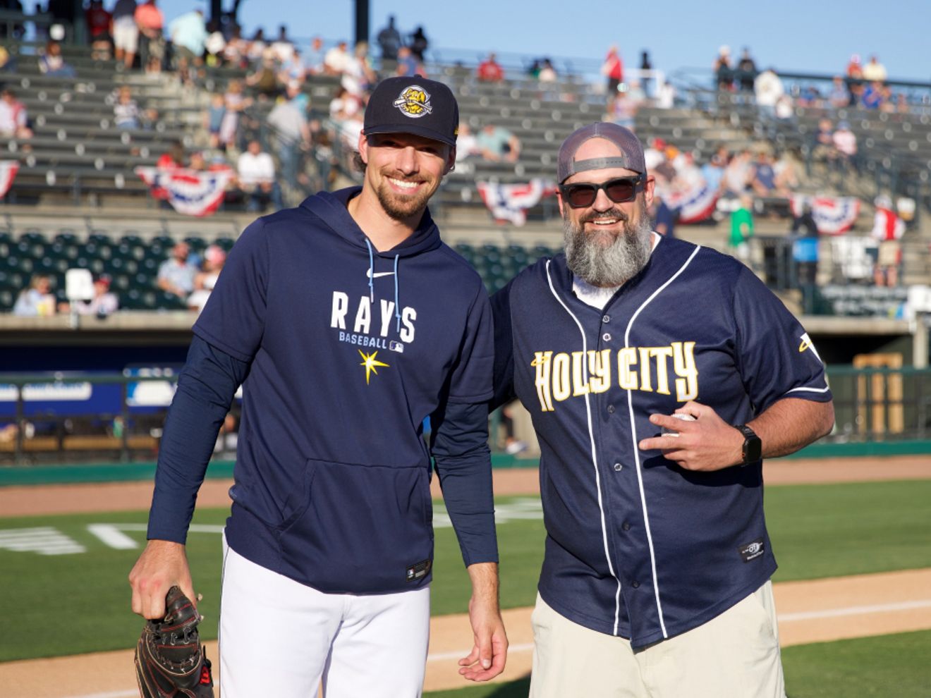 Jon Wellington, veterano de la Marina de EE. UU., está de pie en un campo de béisbol junto a un jugador de béisbol.