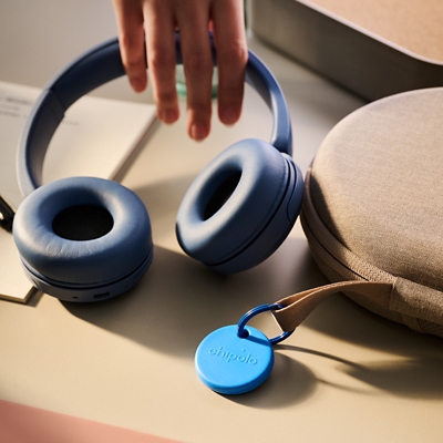 Unos audífonos cerca de un dispositivo de rastreo Chipolo azul.