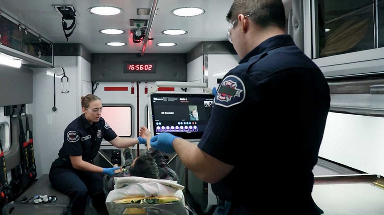 Paramédicos hacen un tratamiento de emergencia dentro de una ambulancia mientras usan herramientas digitales en tiempo real para monitorear y coordinar el tratamiento del paciente.