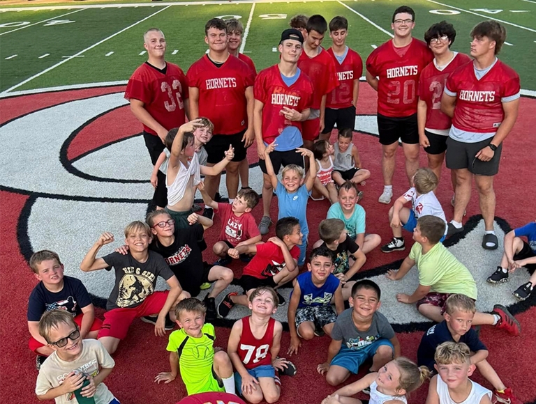 Jugadores de fútbol americano de Crystal City posan con un grupo de niños en el campo de fútbol.